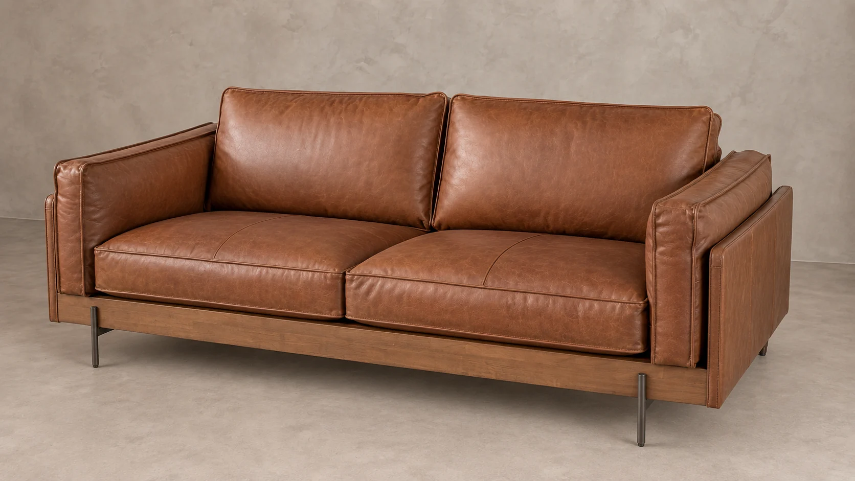 Divano marrone a due posti con rivestimento color cognac, base in legno e piedini sottili in metallo