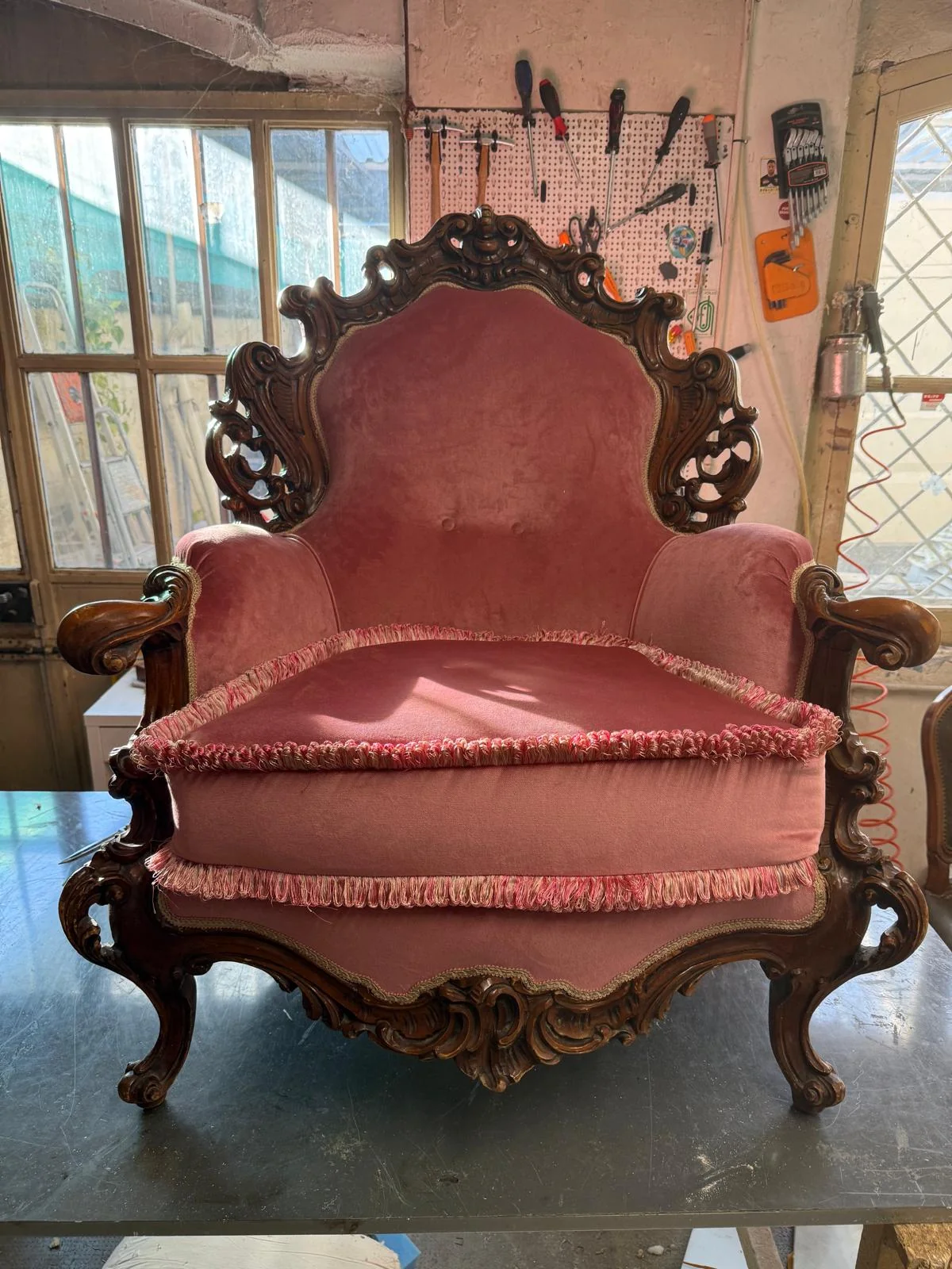 Poltrona in legno intagliato con rivestimento rosa e passamaneria, fotografata sul banco del laboratorio